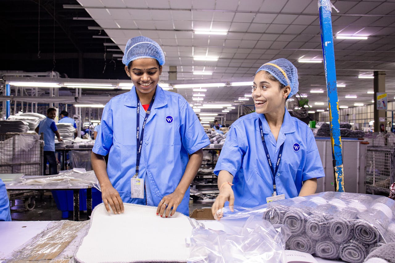 pexels-photo-31112188 Textile warehouse workers in blue uniforms packing materials with smiles.