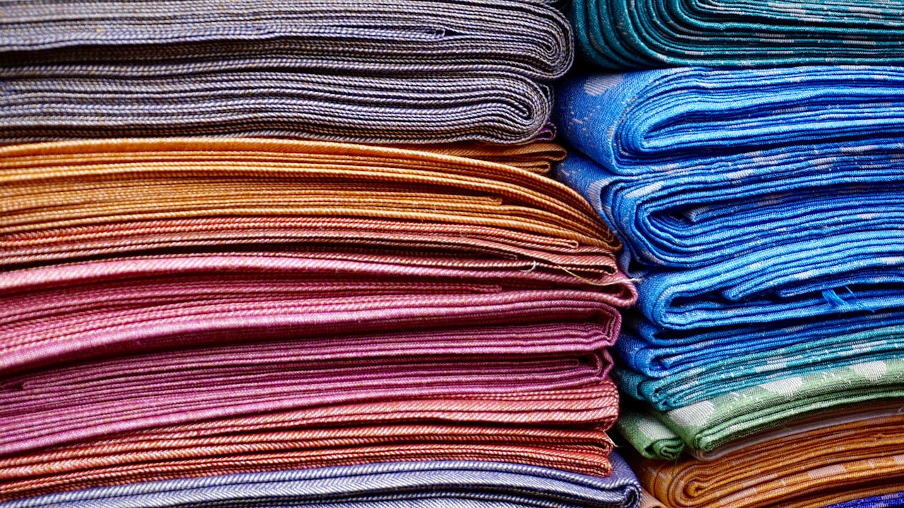 about-02 Vibrant and neatly stacked fabrics showcasing an array of colors and patterns, ideal for fashion and textile design.